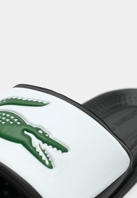 Crna i bijela klizna sandal s reljefnim zeleni krokodil logotipom na remenu.
