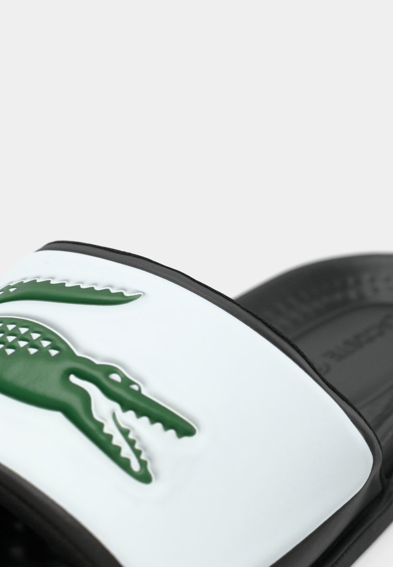 Sandale à glissière noir et blanc avec un logo crocodile en relief vert sur la sangle.