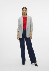 Blazer gris à manches retroussées sur un haut rouge texturé, associé à un jean large marine et des escarpins noirs à bout pointu. Design simple et moderne.