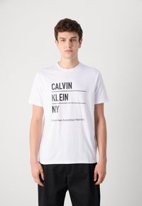 Bijela pamučna majica s crnim tekstom: "CALVIN KLEIN NY" u debelom fontu. Uključuje "Calvin Klein Established 1968 NYC" na dnu.