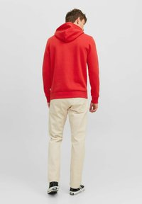 Sudadera con capucha roja, hecha de algodón, diseño ajustado, mangas largas, costuras planas, combinada con pantalones beige claros y zapatillas negras.