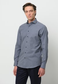 Camicia button-up in tessuto grigio scuro con una sottile texture, dotata di colletto a punta, maniche lunghe e bottoni neri lungo la parte anteriore.