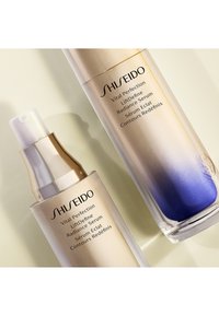 Duo di sieri Shiseido con bottiglia di vetro dorata e azzurro sfumato, dettagli metallici e erogatore trasparente. Etichette stampate chiaramente in nero.