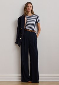Granatowo-biała koszulka w paski zestawiona z granatowymi, szerokimi spodniami z wysokim stanem. Ciemna marynarka zarzucona na jedno ramię. Akcent w postaci brązowego paska.
