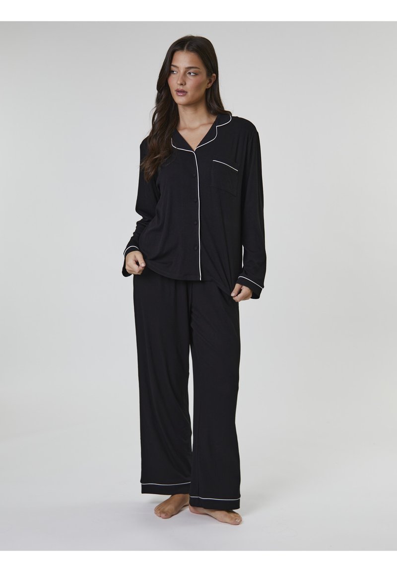 Svart pyjamasset av mjukt tyg, med en knapp-up skjorta med ficka och vit piping, kombinerat med matchande, löst sittande byxor.