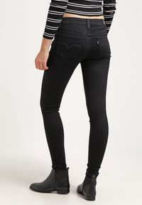 Jeans skinny negros con cintura alta, hechos de denim elástico. Presentan dos bolsillos traseros con detalles de costura y una pequeña etiqueta de la marca en la cinturilla.