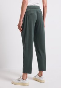 Zielone, luźne spodnie wykonane z miękkiego materiału, z dwiema tylnymi kieszeniami i szerokim paskiem w talii. Połączone z białymi trampkami.