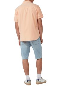 Korte mouw, lichtoranje shirt met een kraag, gecombineerd met lichtblauwe denim shorts en witte sneakers met marineblauwe accenten.