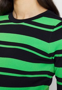 Schwarz-grün gestreiftes Stricktop mit rundem Halsauschnitt. Verfügt über breite horizontale Streifen in verschiedenen Breiten. Estrukturierter Stoffabschluss.