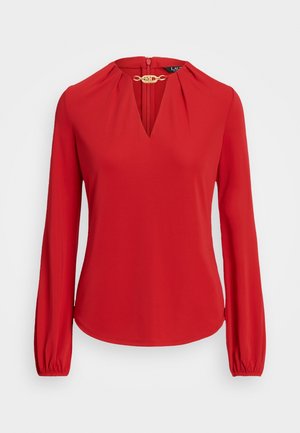 Blusa rossa a maniche lunghe con scollo a V e fermaglio decorativo dorato al colletto, con dettagli arricciati e polsini elastici.