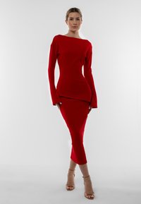 Abito rosso a coste con silhouette aderente, scollatura a barca e maniche lunghe. Il materiale è liscio; il design include un orlo a strati.