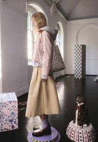 Mladá žena s kvetinovou taškou stojí na fialovom kruhovom podstavci v galérii s ozdobnými sochami a oblúkovými oknami.