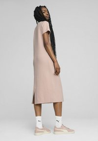 Robe rose à manches courtes, mi-longue, avec une coupe droite et des fentes sur les côtés, portée avec des baskets rose clair et des chaussettes blanches hauteur genou.