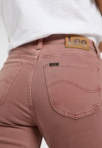 Jeans de mezclilla rosa con una textura suave, que cuentan con bolsillos traseros curvados y un parche de cuero de la marca Lee en la cinturilla.