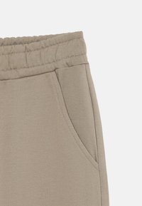 Pantalons de survêtement beiges avec une taille élastique, poche latérale et texture lisse. Présente des détails cousus le long de la taille et de la poche.