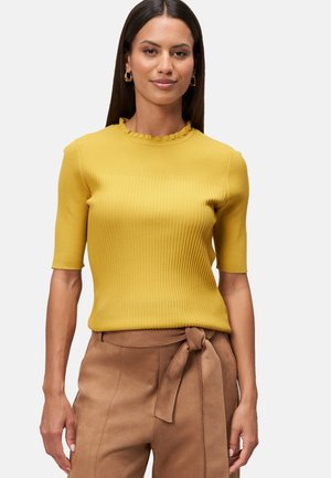 Haut en tricot à côtes jaunes avec un col en forme de vagues et des manches courtes, associé à un pantalon brun taille haute avec un détail de ceinture nouée.