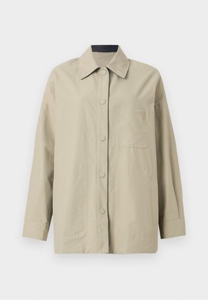 Veste oversize beige en tissu léger, avec un col pointu, une fermeture à boutons sur le devant et une poche poitrine avec un détail de logo en relief.