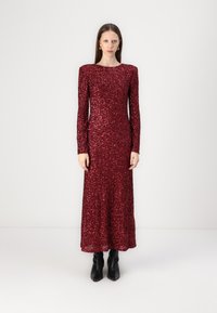 Red sequined long dress with long sleeves and a rounded neckline, featuring a fitted silhouette and a floor-length hem. Black ankle boots.