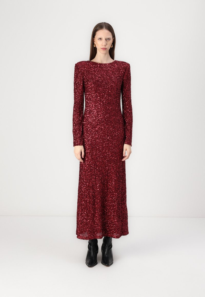 Red sequined long dress with long sleeves and a rounded neckline, featuring a fitted silhouette and a floor-length hem. Black ankle boots.