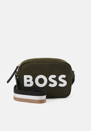 Bolsa rectangular verde oliva con texto blanco "BOSS" y correa ajustable multicolor en negro, blanco y marrón sobre un fondo blanco.
