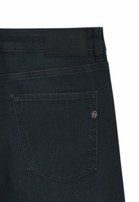 Mörkblå denimjeans med bakfickor, en svart läderpatch med BOSS-logotyp och ett litet metallpin-badge med dubbel-B emblem på fickkanten.