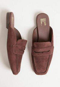 Un paio di mocassini in suede marrone, slip-on, con tacco basso e punte quadrate, caratterizzati da un dettaglio a strappo sulla parte superiore e il testo "amici come questi..." sulle solette.
