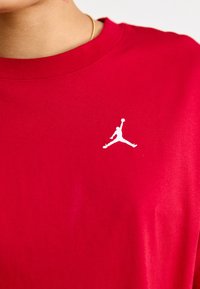 Raudona medvilninė marškinė su apvaliu iškirpimu, ant kairiojo krūtinės ploto turi spausdintą baltą Jordan logotipą. Glotni tekstūra.