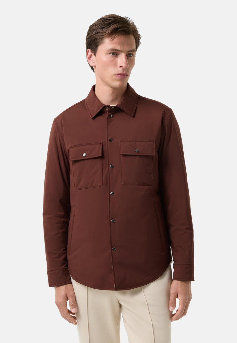 Braune, knöpfbare Jacke mit langen Ärmeln, zwei Brusttaschen und einem spitzen Kragen. Glatte Textur und minimalistische Designakzente.
