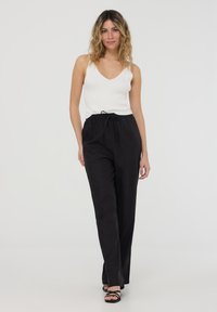 Pantaloni neri, larghi, con vita elastica e lacci regolabili, abbinati a un top in cotone bianco a coste.