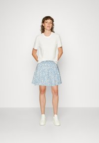 Weißes Kurzarm-T-Shirt kombiniert mit einem blauen Rock mit floralem Muster, der eine ausgestellte Form hat. Abgerundet mit weißen Turnschuhen.