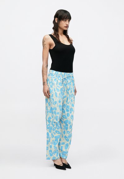 Μαύρο αμάνικο τοπ συνδυασμένο με χαλαρά, ανοιχτό μπλε παντελόνια με σχέδια και κορδόνι στη μέση. Το μοντέλο φοράει μαύρα μυτερά φλατ παπούτσια.
