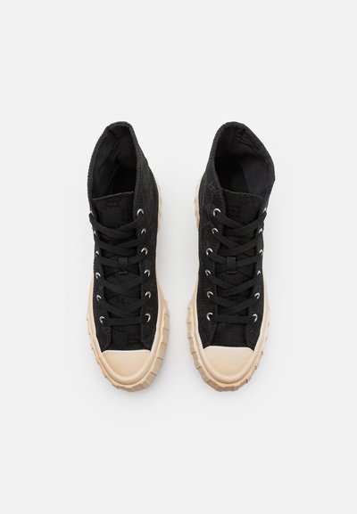 Adidași negri tip high-top cu o suprafață texturată, vârful rotund și o talpă din cauciuc bej. Au șireturi negre și gauri metalice pentru șireturi.