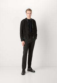 Mustat farkkutakki hopeisella vetoketjulla, yhdistetty mustan pyöreäkauluksisen paidan ja mustien slim fit -housujen kanssa. Mustat nahkakengät täydentävät asukokonaisuuden.
