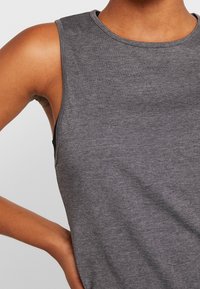 Šedé tílko bez rukávů z měkké a strukturované tkaniny. Má kulatý výstřih a hladké švy, zobrazuje se paže pro detail střihu.