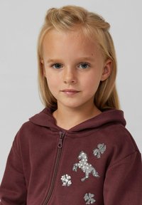 Bordeauxfarbener Zip-Hoodie mit Kapuze, versehen mit silbernen Pailletten-Designs von einem Pferd und Blumen auf der Brust. Weiches, bequemes Material.