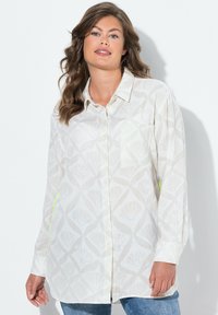 Langarm, knoop-overhemd in lichtcrème met een bladerenpatroon. Beschikt over een zak en groene accenten aan de zijkant, gemaakt van zachte stof.