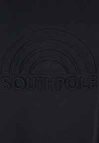 Mustapaita, jossa on kohokuvioitu sateenkaari ja sana "SOUTHPOLE" rohkeilla kirjaimilla kaaren alla.