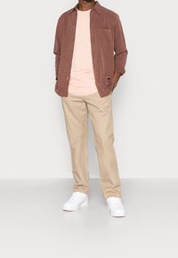 Light brown corduroy shirt over a pale pink t-shirt, paired with beige pants and white sneakers with pink accents.