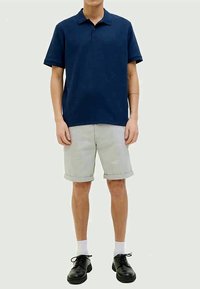 Polo em tom de marinho com mangas curtas, combinado com calções curtos cinza claro arregaçados, meias brancas e sapatos pretos com atacadores. Design simples e casual.