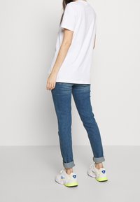 Biała bawełniana koszulka z krótkim rękawem, w połączeniu z niebieskimi dżinsami i białymi trampkami z żółtymi akcentami i niebieskim logo.