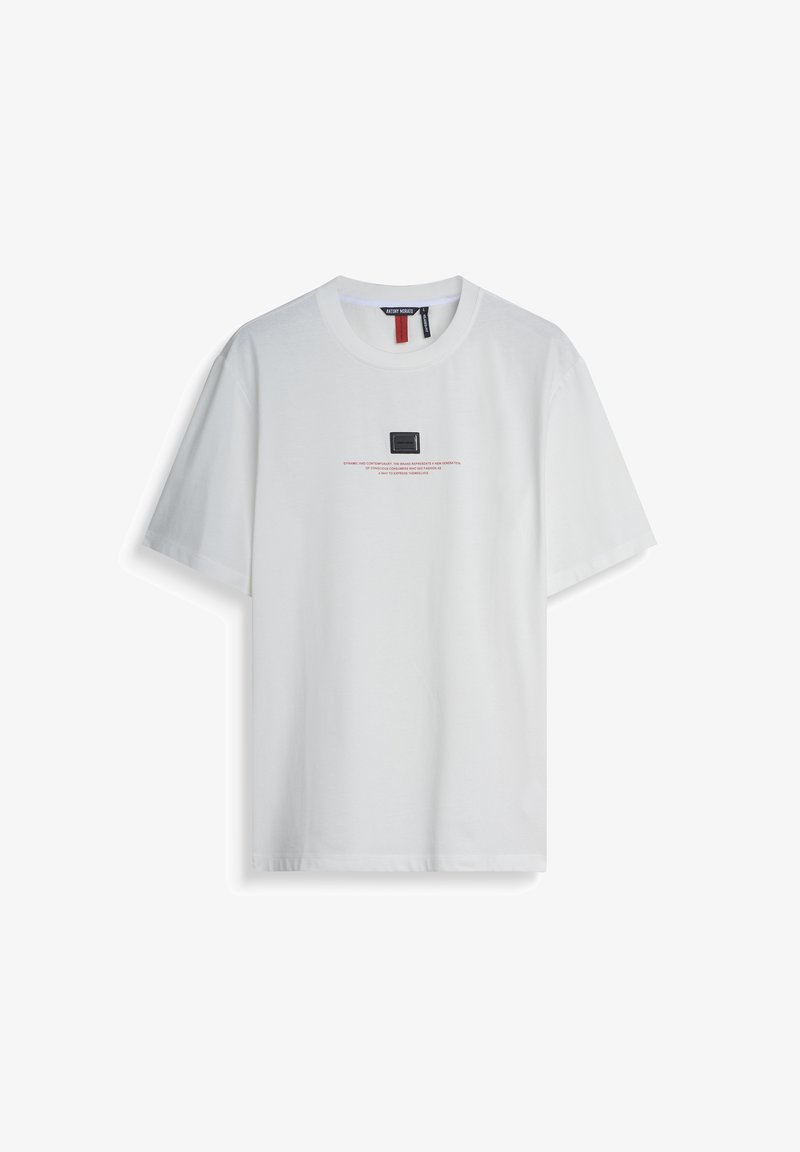 Camiseta de algodón blanca con mangas cortas, que presenta un parche cuadrado negro y texto rojo en la parte delantera. Cuello redondo clásico, corte relajado.