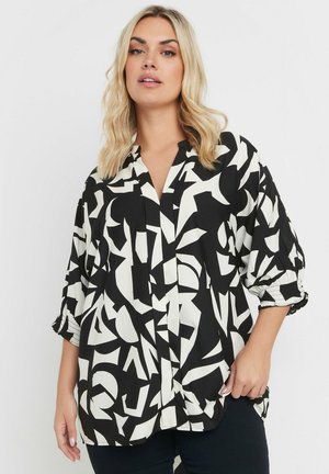 Blusa bianca e nera con motivi geometrici astratti, maniche lunghe con polsini arricciati e chiusura con bottoni. Tessuto leggero.