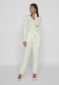 Heled beež v-kaelusega sviiter ja sobivad kõrge vöökohtaga püksid, millel on nöörvöö. Sile tekstuur, figureeritud lõige ja teravad kontsad.