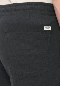 Σκούρο γκρι παντελόνι φόρμας με υφή υφάσματος, διαθέτει ελαστική μέση και πίσω τσέπη με μικρή ετικέτα μάρκας.