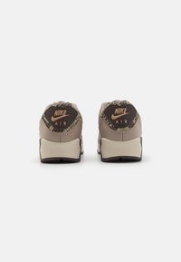 Svijetlosmeđi Nike Air tenisice s teksturiranim akcentima na peti, crnom gumiranom potplatu i detaljem loga na stražnjem dijelu. Elegantan dizajn s kontrastnim bojama.