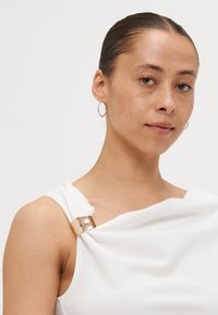 Witte draperingstop met een metallic gouden accent op de schouder. Gladde textuur met een modern, minimalistisch ontwerp.