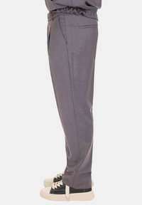 Pantaloni grigi sartoriali con una vestibilità rilassata, caratterizzati da una texture liscia, tasche laterali e una cintura elastica, abbinati a sneakers nere e crema.