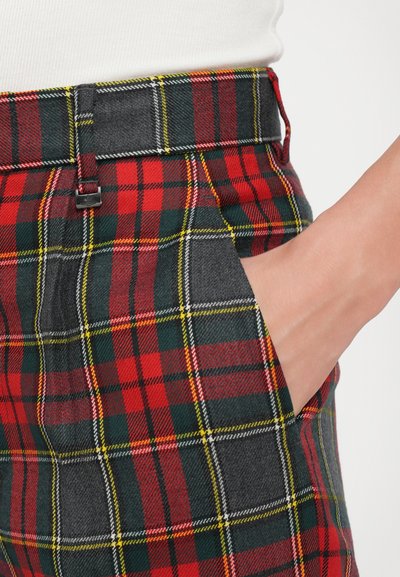 Red, green, and black plaid trousers made of fabric with a smooth texture. Features include a belt, side pocket, and contrasting stitching details.