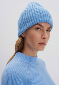 Cappello a cuffia azzurro chiaro in maglia con coste verticali e parte superiore conica. Indossato con un maglione testurizzato coordinato, entrambi realizzati in filato leggero.