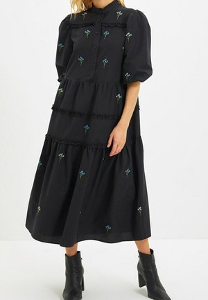 Zwarte midi-jurk met pofmouwen, knoopsluiting aan de voorkant, kleine blauwe en witte bloemmotieven en ruches, gedragen met zwarte enkellaarsjes met hak.